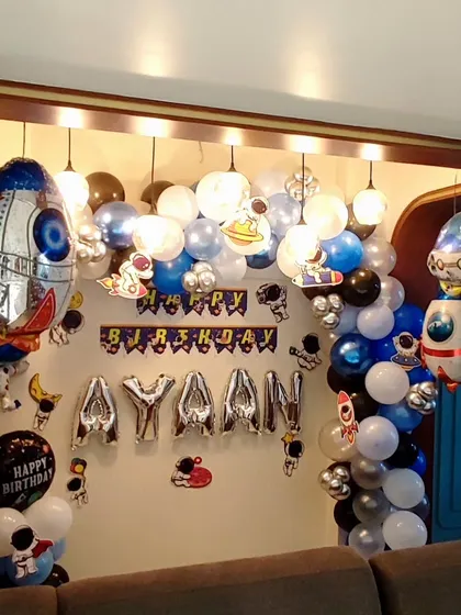 An out-of-this-world space-themed birthday party. This decoration includes a balloon garland with blue, white, black, and silver balloons to represent the galaxy. I added large rocket ship foil balloons, astronaut cutouts, and the birthday boy's name "AYAAN" in silver foil letters to complete the cosmic adventure.