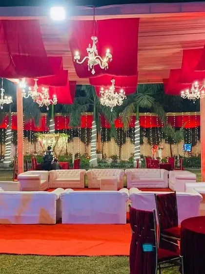 A comfortable white lounge sofa arrangement on a red carpet for a grand wedding. The area is set under a canopy of red drapes and chandeliers, perfect for guests to relax.