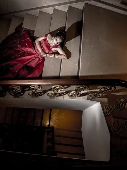 An artistic, high-angle shot of a bride in a red gown, looking up from the bottom of a staircase.