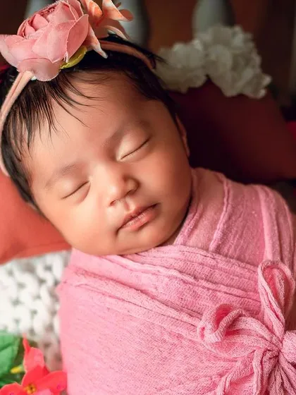 A close-up of a baby wrapped in pink, surrounded by flowers. This angle allows us to capture the sweet details of their face while they sleep.