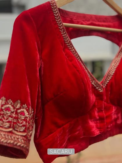 A vibrant red velvet blouse with a deep V-neck and zardosi embroidery on the sleeves, perfect for brightening up any festive saree.