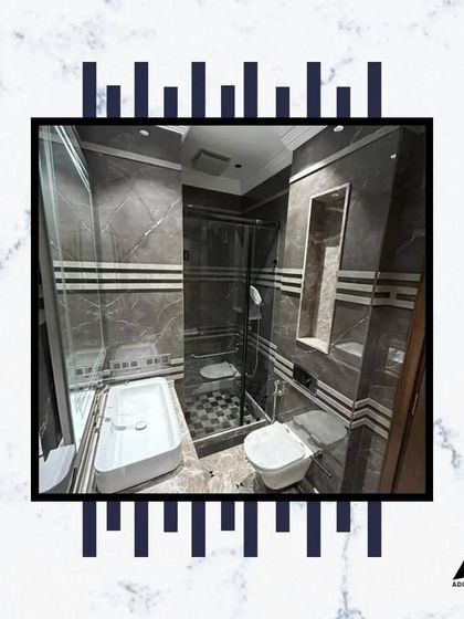 This bathroom features a spacious walk-in shower with a glass partition. The combination of dark marble walls with patterned tile inlay adds texture and visual interest.