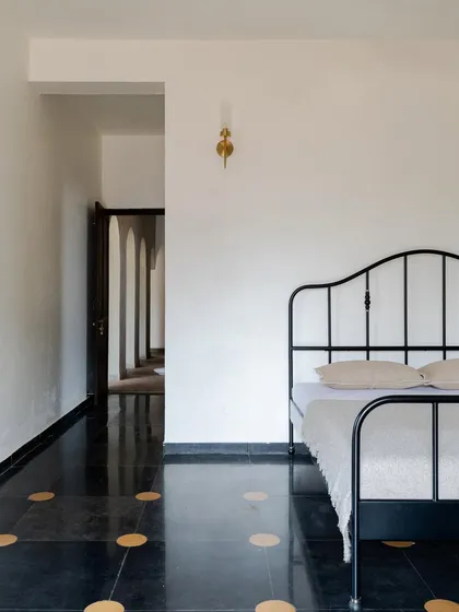 The flooring in Maison Rouge is a key design element, featuring black stone with striking yellow circular inlays. This detail, seen here in a minimalist bedroom, adds a touch of modern graphic design to the otherwise traditional space.