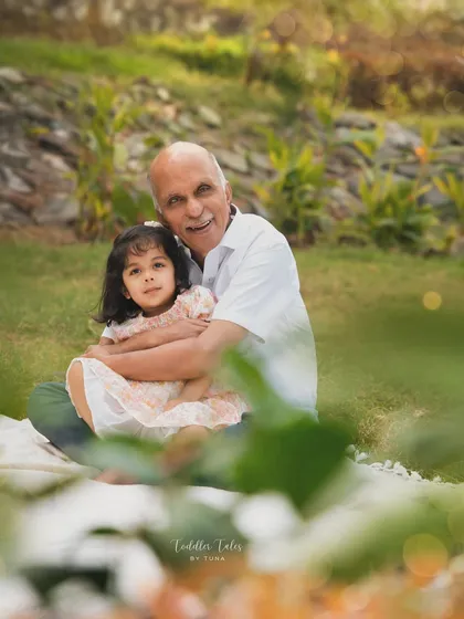 A grandfather shares a gentle hug with his granddaughter in a beautiful park setting. These portraits are treasured keepsakes of the special bond between generations.