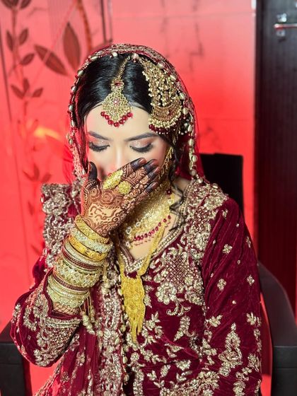 A gorgeous Nikkah bride in a deep maroon velvet outfit. Her makeup is bold and dramatic, with smokey eyes and heavy gold jewelry.