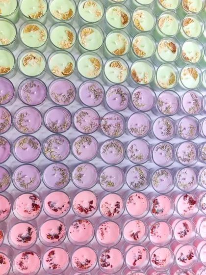 A Rainbow of Possibilities. This is what a large custom order looks like before it heads out. Rows of colorful votive candles, each topped with unique botanicals like dried lime, lavender, and rose petals, show the scale and variety I can offer for your brand or big event.
