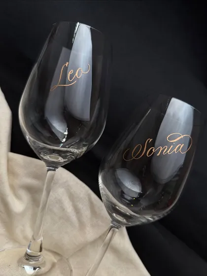 A pair of wine glasses engraved with the names 'Leo' and 'Sonia'. The gold-filled engraving stands out beautifully against the dark backdrop, creating a luxurious feel.