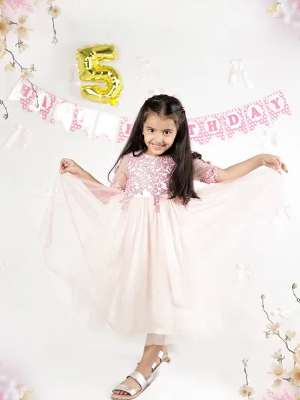 A princess celebrating her fifth birthday. Dressed in a beautiful pink gown, she is twirling in front of a birthday banner in our studio.