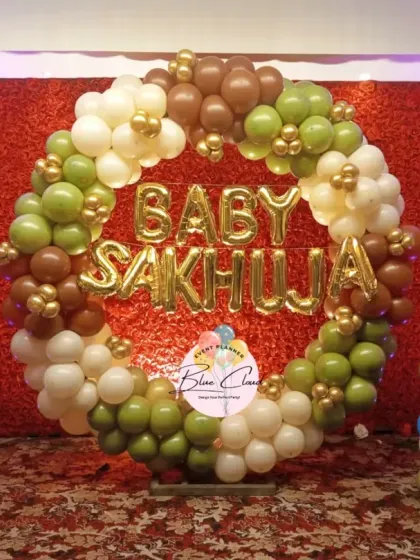 A baby shower decoration with a balloon ring in earthy tones of green and brown, with the family name in foil letters.