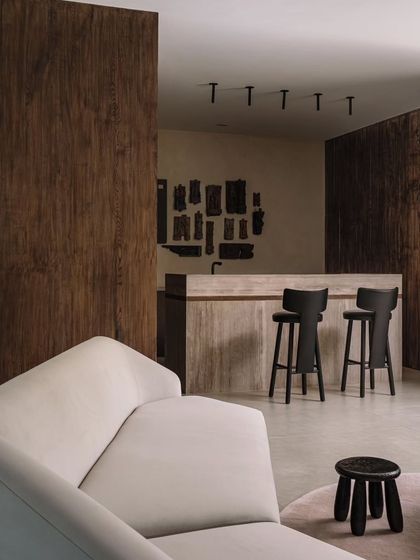 The bar area within the living room, featuring a travertine counter and dark wood paneling. The space is decorated with an installation of old wooden printing blocks, adding a touch of history and craft.