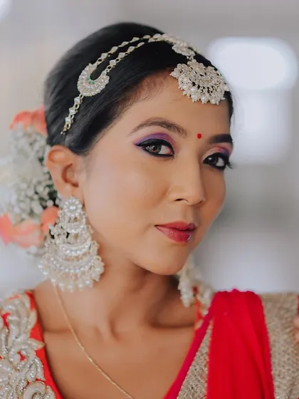 A close-up portrait of a model in a red lehenga, showcasing her elaborate makeup and jewelry. The soft focus and direct gaze create a powerful and beautiful image.