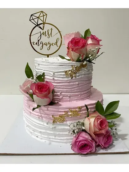 A classic and elegant two-tier engagement cake. This 3kg cake features a textured pink and white ombre design, decorated with fresh roses and a "Just Engaged" topper.