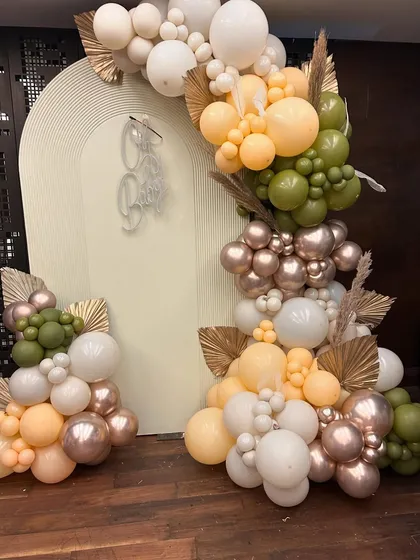 An elegant baby shower setup featuring an 'Oh Baby' neon sign and a beautiful organic balloon arch in earthy tones of olive green, peach, and metallic rose gold.