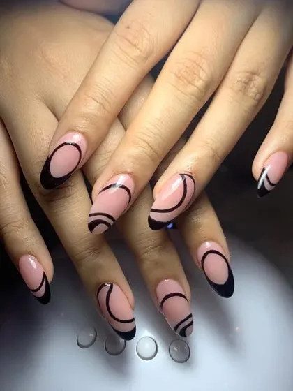 A minimalist yet edgy design with a nude base and abstract black outlines on oval-shaped nails.