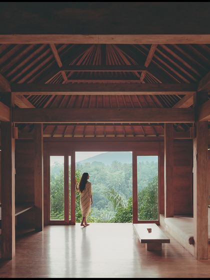 A shot from the 'Pause' campaign, where the model looks out from a beautiful wooden villa into the jungle. The image evokes a sense of peace and connection with nature.