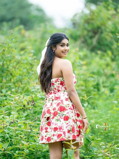 A back view of a model in a floral dress, walking through a green field.