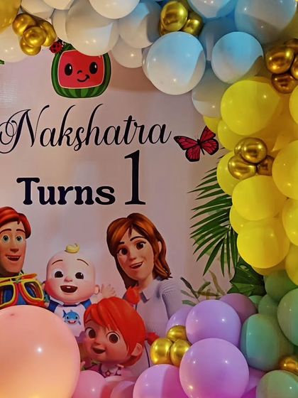 A close-up of a Cocomelon-themed first birthday backdrop, featuring the whole family and a colorful balloon garland.