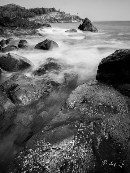 This is the same dramatic seascape as the featured image ID 1, offered here as a print. The black and white format enhances the contrast between the smooth water and the rugged, textured rocks.