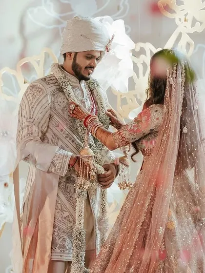The varmala moment for Yasha and Rahil, captured against a backdrop of giant, handcrafted paper flowers. This artistic installation provided a unique and ethereal setting for their exchange of garlands.