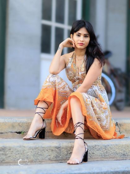 An elegant and poised seated portrait on outdoor steps. The flowing paisley dress and strappy heels create a sophisticated and stylish look.