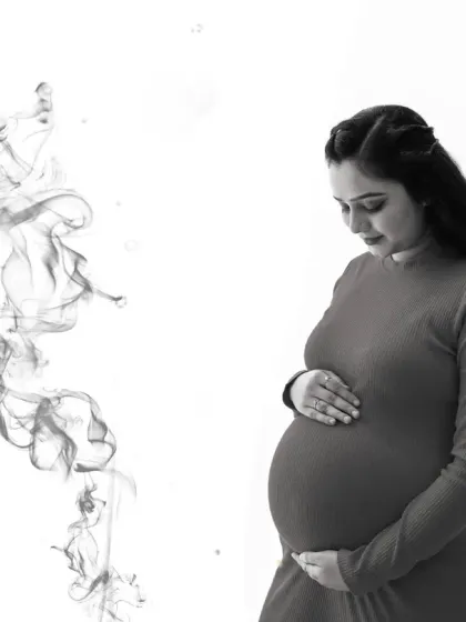 A serene and artistic black and white portrait. The mom-to-be looks down at her bump, with a wisp of smoke-like effect adding a creative and ethereal touch to the image.