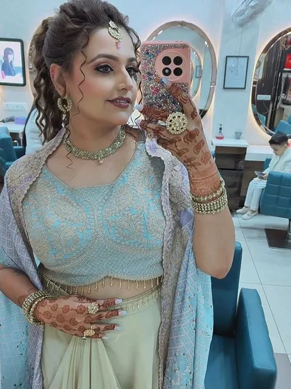 A happy client taking a selfie in our salon. She's rocking a curly ponytail and glowing makeup for her party, with beautiful henna on her hands.