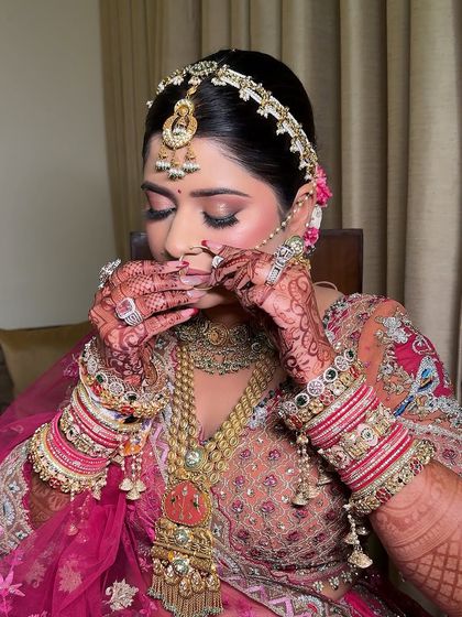 A close-up of the bride's hands and face, showing the beautiful henna and the delicate nath. The soft pink makeup ties the whole look together.