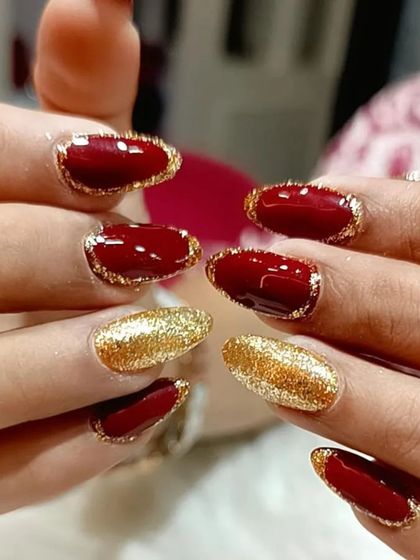 A festive and glamorous set featuring deep red nails with a gold glitter border, paired with full-coverage gold glitter accent nails.