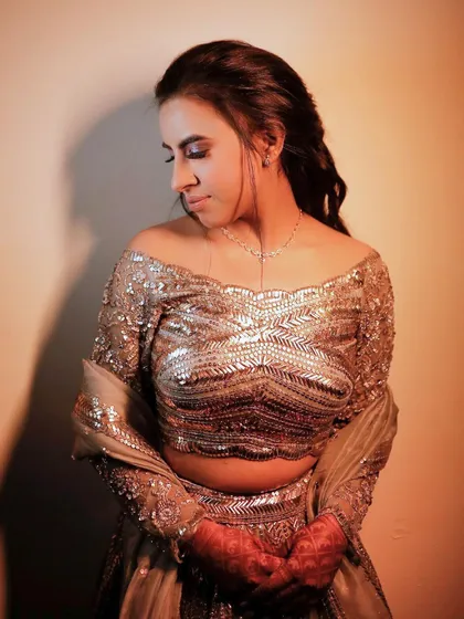 A poised portrait of the bride-to-be, looking down gracefully. The lighting highlights the texture and sparkle of her heavily embellished blouse.