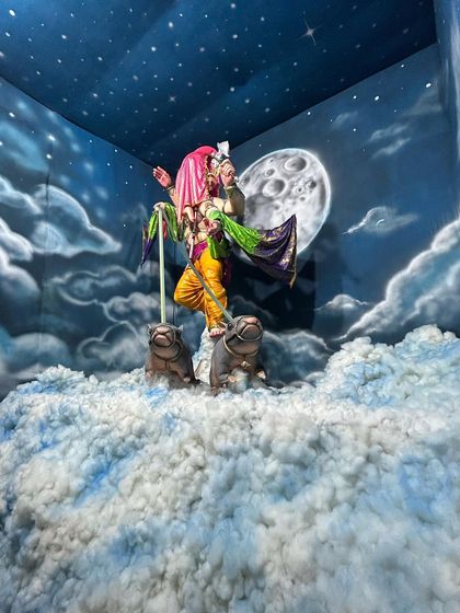 A wide-angle view showing how the painted backdrop and the physical decorations come together to create a divine scene for the Ganpati idol.