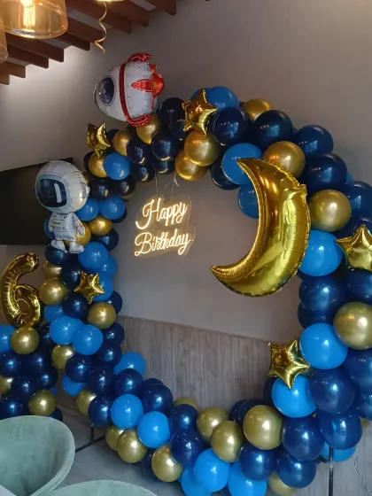 A space-themed balloon ring in blue and gold with a crescent moon, astronaut, and rocket ship foil balloons.