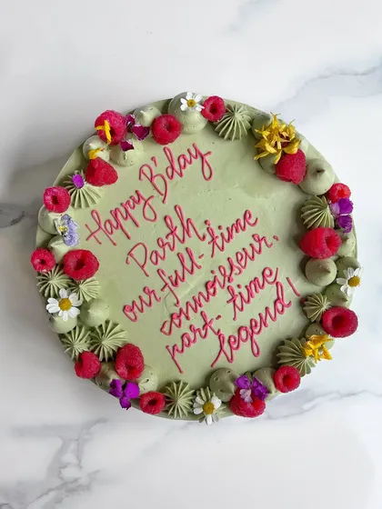 A top-down view of the Pistachio Raspberry cake, showing the beautiful contrast between the pistachio green frosting, bright red raspberries, and delicate edible flowers.