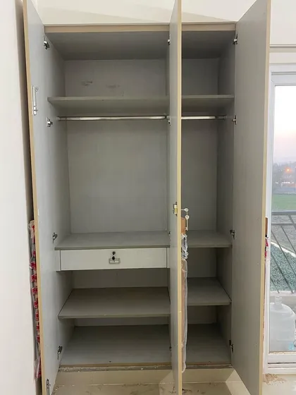The inside of a three-door wardrobe, designed for maximum utility with a mix of hanging space, shelves, and a lockable drawer.
