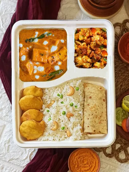 This is a sample of our executive veg thali, perfect for corporate lunches. It includes creamy Paneer Makhani, Aloo Gobi, fragrant Peas Kaju Rice, soft Chapati, and crispy Aloo Pakodas, all packed in a convenient, biodegradable tray.