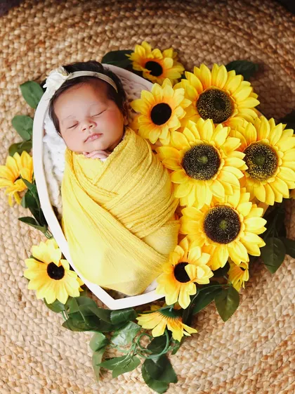 An overhead shot of a newborn surrounded by a halo of bright sunflowers. The yellow wrap and natural jute mat complete this sunny and cheerful setup.