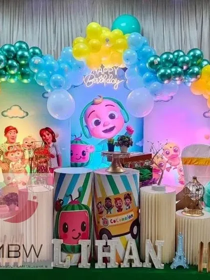 This Cocomelon party uses bold shades of blue and green, with a large character head as the centerpiece of the backdrop, creating a high-impact visual.