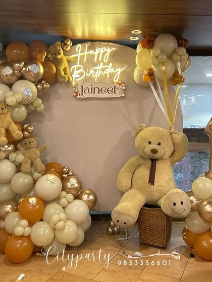 A full view of the teddy bear first birthday setup, including the balloon arch with small teddy bears tucked in and a balloon column with a number '1' foil balloon.