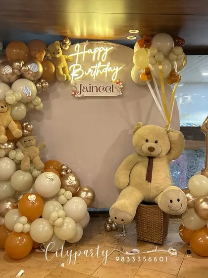 A full view of the teddy bear first birthday setup, including the balloon arch with small teddy bears tucked in and a balloon column with a number '1' foil balloon.