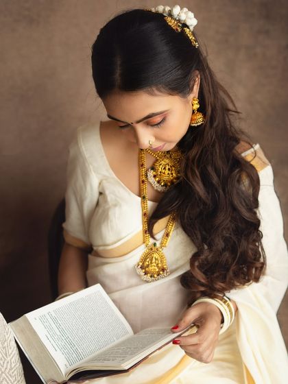 A quiet, contemplative moment. This close-up captures the intricate details of the traditional temple jewelry and the serene expression of the mom-to-be as she reads from a holy book.