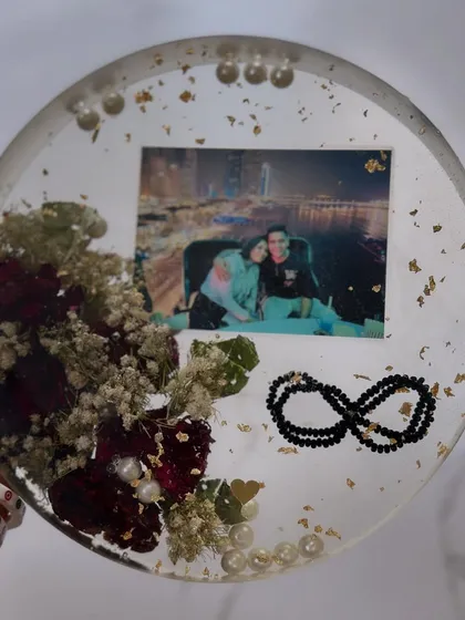 A circular keepsake preserving a photo, flowers, and a delicate black bead bracelet. A beautiful way to keep multiple memories together.