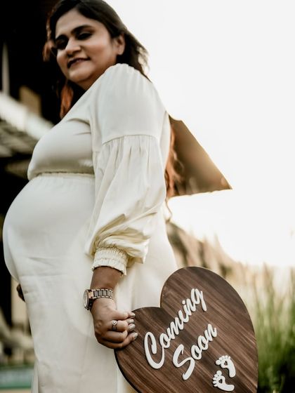 A low-angle shot of the mom-to-be holding a "Coming Soon" sign, emphasizing the baby bump and the anticipation of the new arrival.