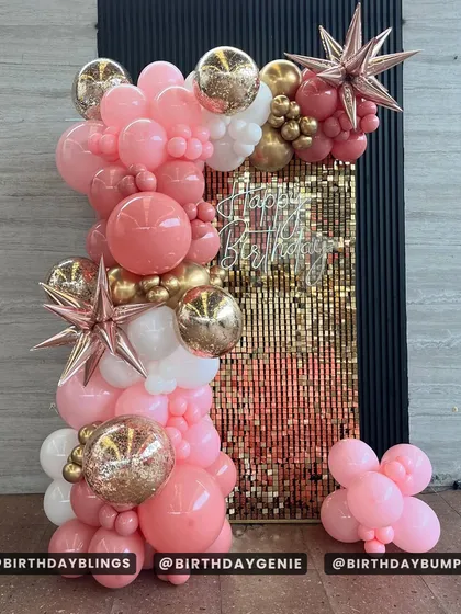 A beautiful rose gold and pink balloon column against a gold shimmer wall. The starburst and glitter-filled balloons add extra sparkle and texture.