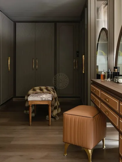 This classic walk-in closet features dark wood wardrobes with diamond-patterned details and elegant brass handles. A leather-upholstered vanity stool adds a touch of warmth and luxury.
