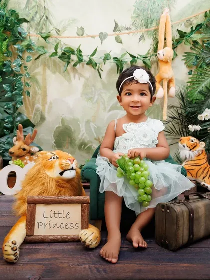 A little princess in her jungle kingdom, sitting on a miniature green chair with a lion by her side.