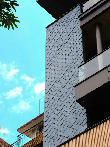 A detail of the fish-scale shingles, showcasing their texture and how they catch the light. This element adds a unique, organic pattern to the modern facade.