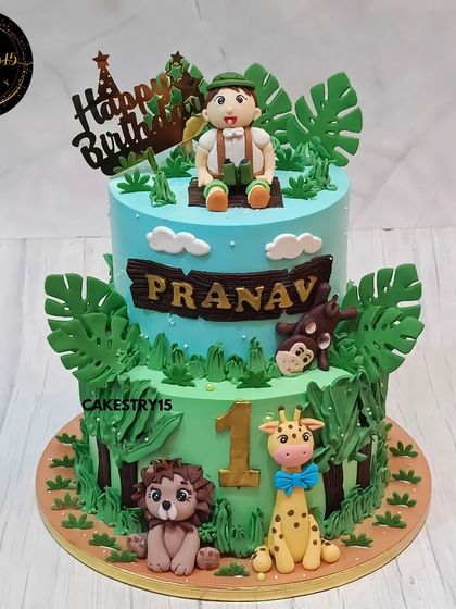 A fun two-tier jungle safari cake for a first birthday. This 3kg pineapple cake features a boy figurine, a lion, a giraffe, and a monkey.
