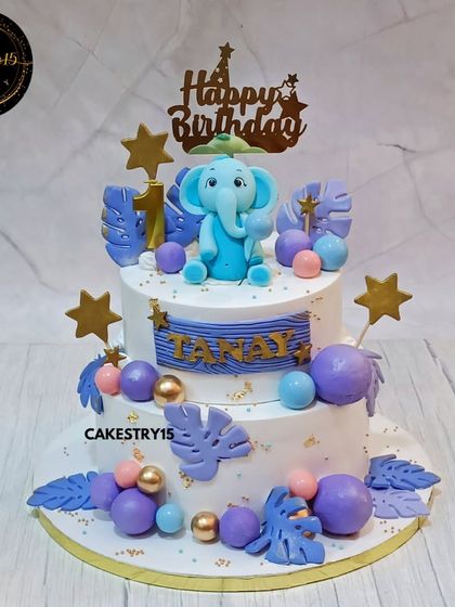 An adorable two-tier elephant-themed cake for a first birthday. This blueberry cake is topped with a cute 3D fondant elephant and decorated with purple and blue spheres.