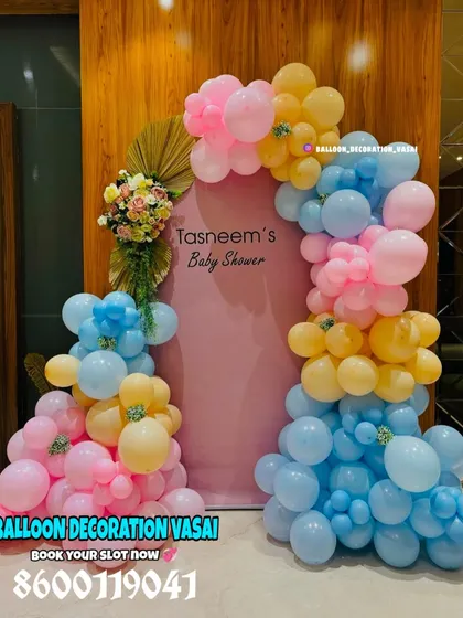 A bright and cheerful baby shower backdrop using a pastel palette of pink, blue, and yellow. The custom arched board with the mother's name makes the decoration feel personal and special.