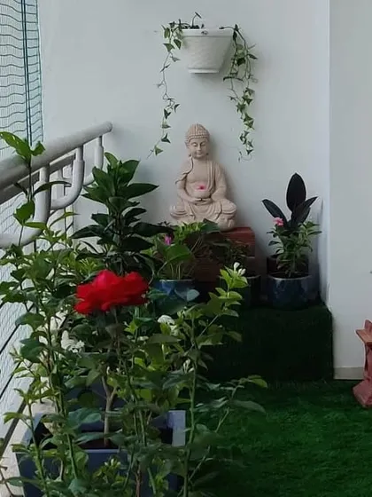 A tranquil corner of a balcony we designed, featuring a Buddha statue, artificial grass, and a mix of flowering and foliage plants, including a beautiful red rose.