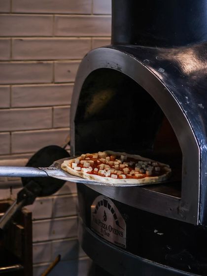 Pizza in progress. A pizza loaded with cheese is carefully placed into the fiery oven with a peel.